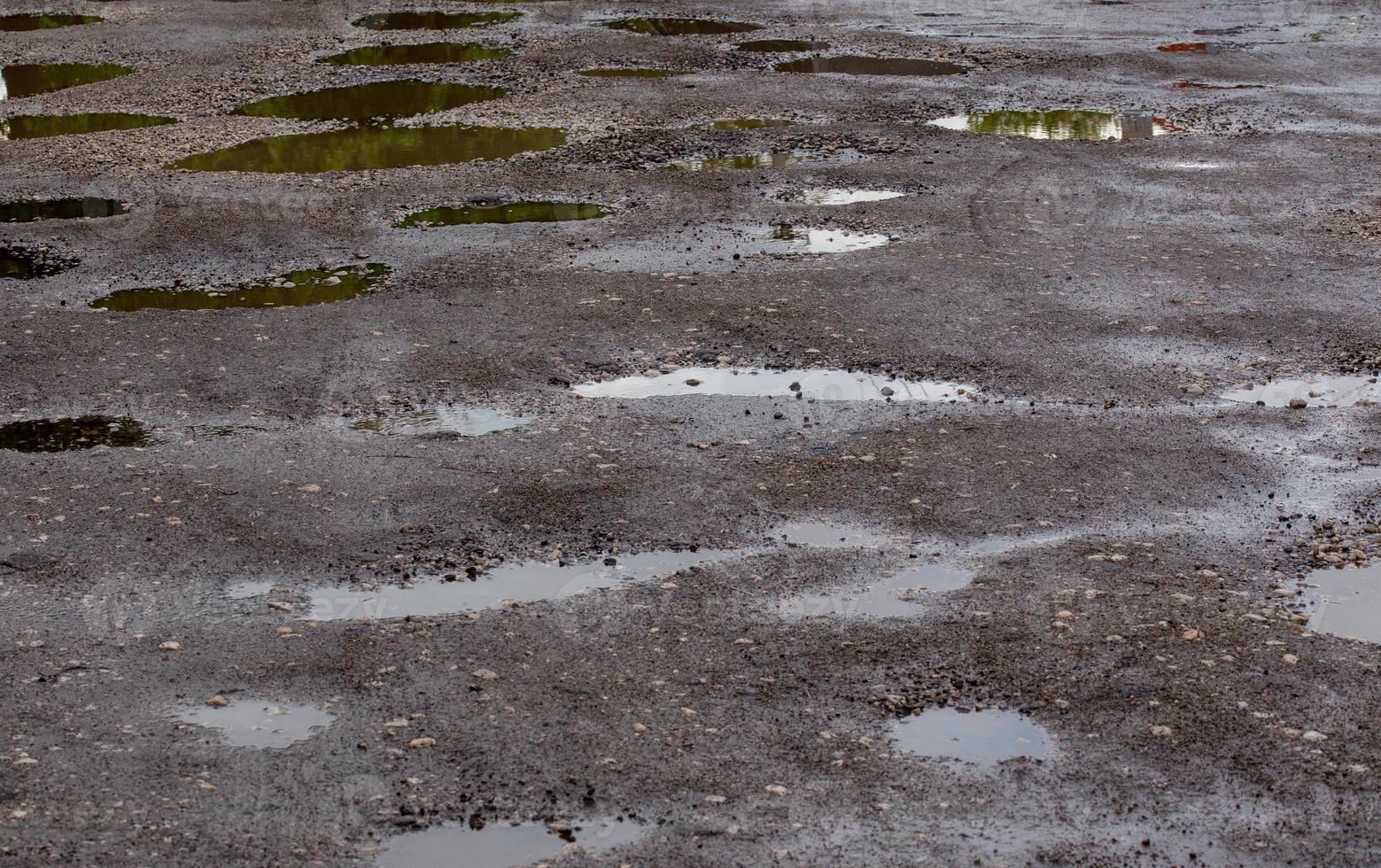 asfalto de carretera dañado con baches con múltiples charcos después de la lluvia durante el día de verano foto