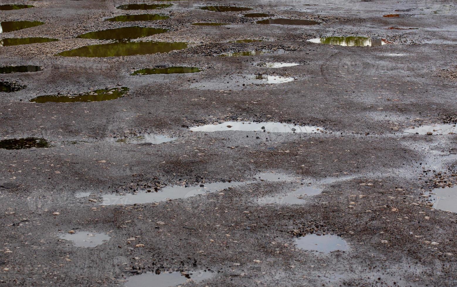 bumpy damaged road asphalt with multiple puddles after rain at summer daytime photo