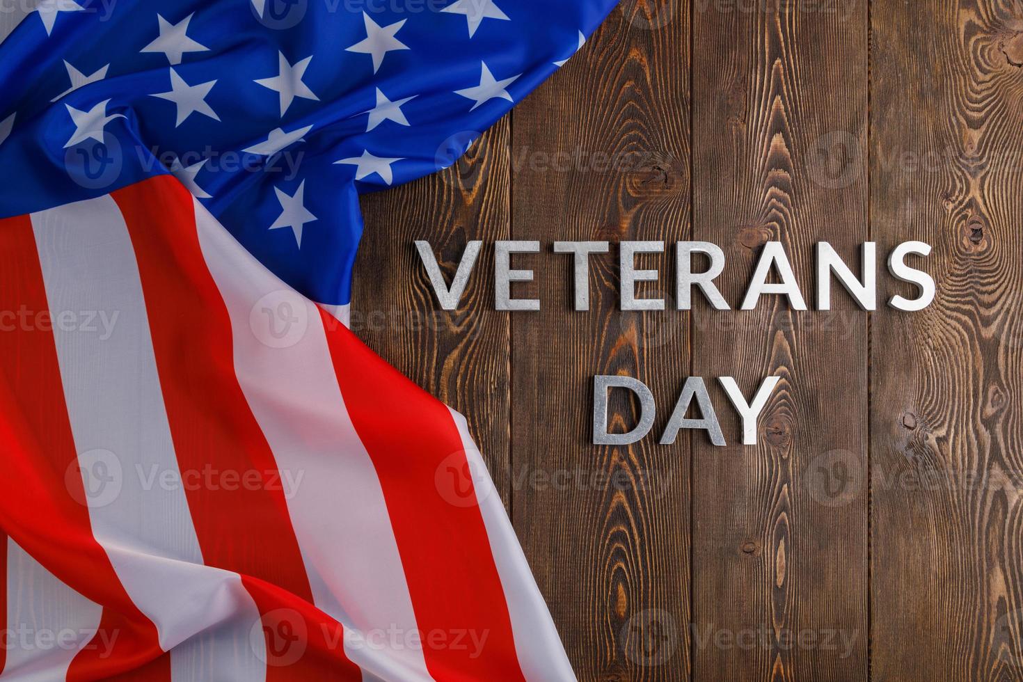 the words veterans day laid with silver metal letters on wooden board surface with crumpled usa flag photo