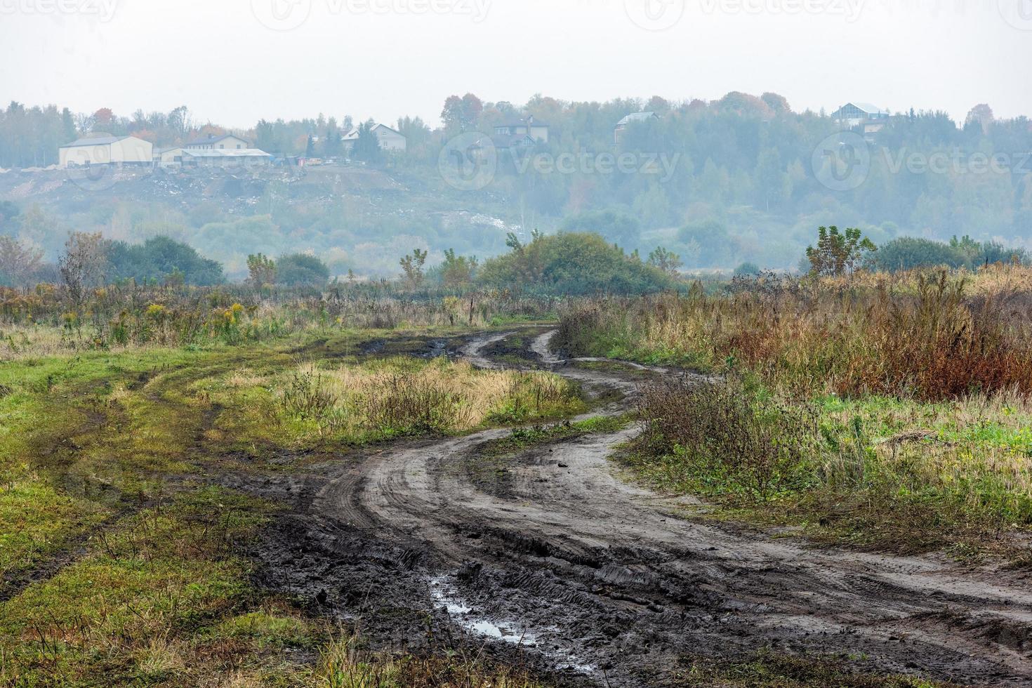 autumnal foggy morning rustic lansdcape with dirt road in the foreground and small buildings on hill in the background photo