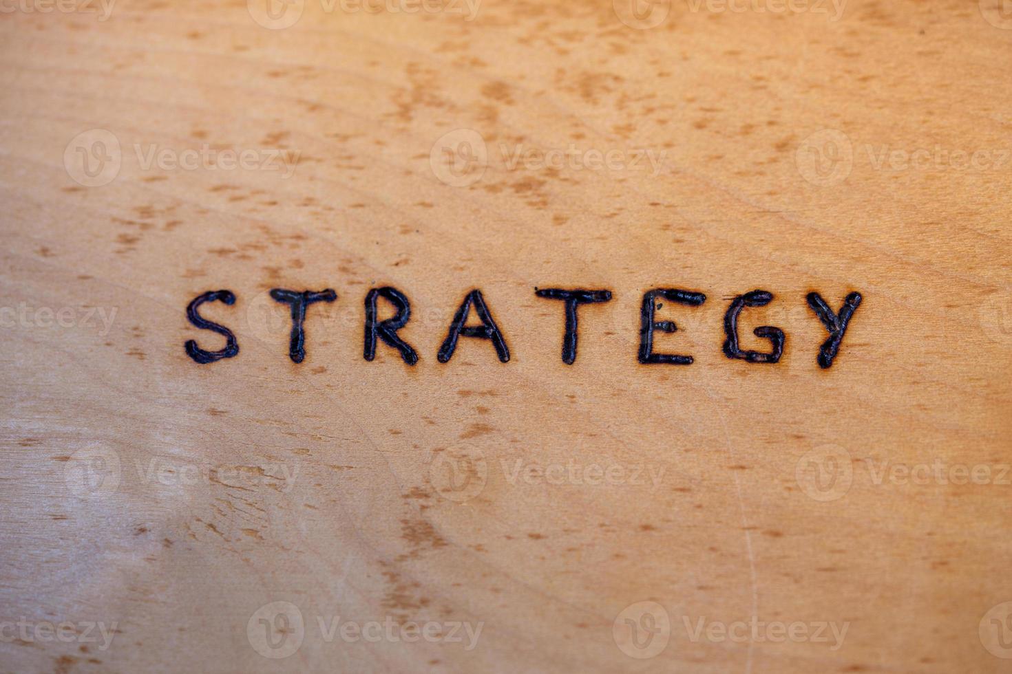 the word strategy handwritten on flat bare plywood surface with woodburner photo