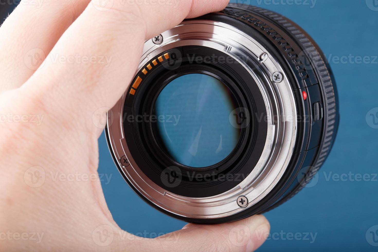 hand holding modern digital 50 mm f 1.4 dslr lens on blue background - close-up view on bayonet with selective focus photo