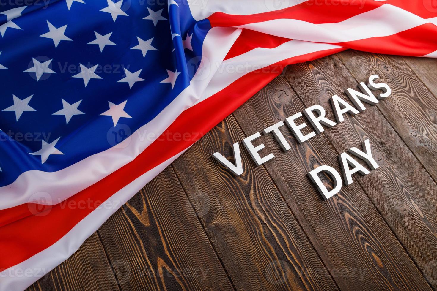 the words veterans day laid with silver metal letters on wooden board surface with crumpled usa flag at right side with diagonal perspective photo