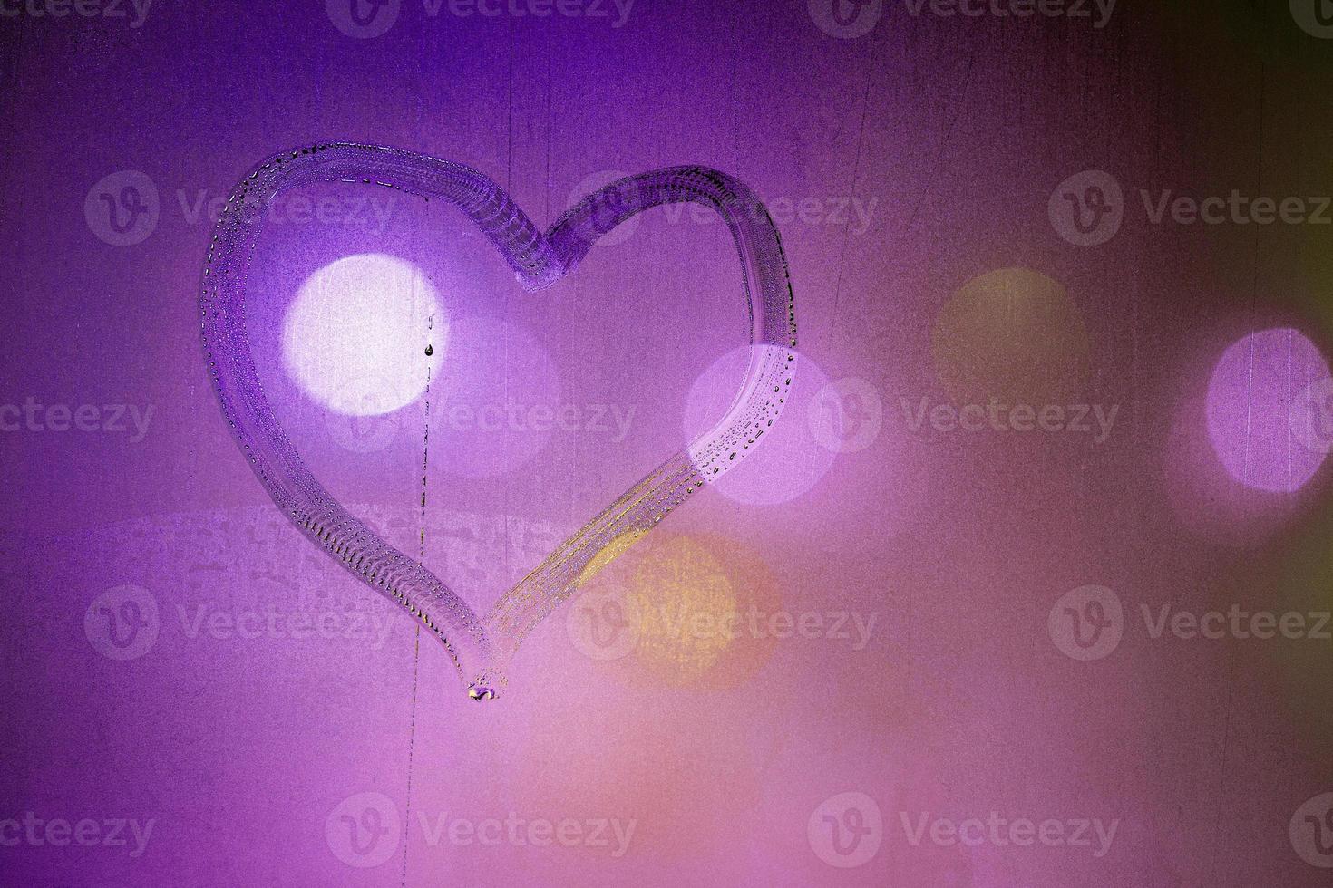 heart symbol hand drawn on wet night window glass in pink colors photo