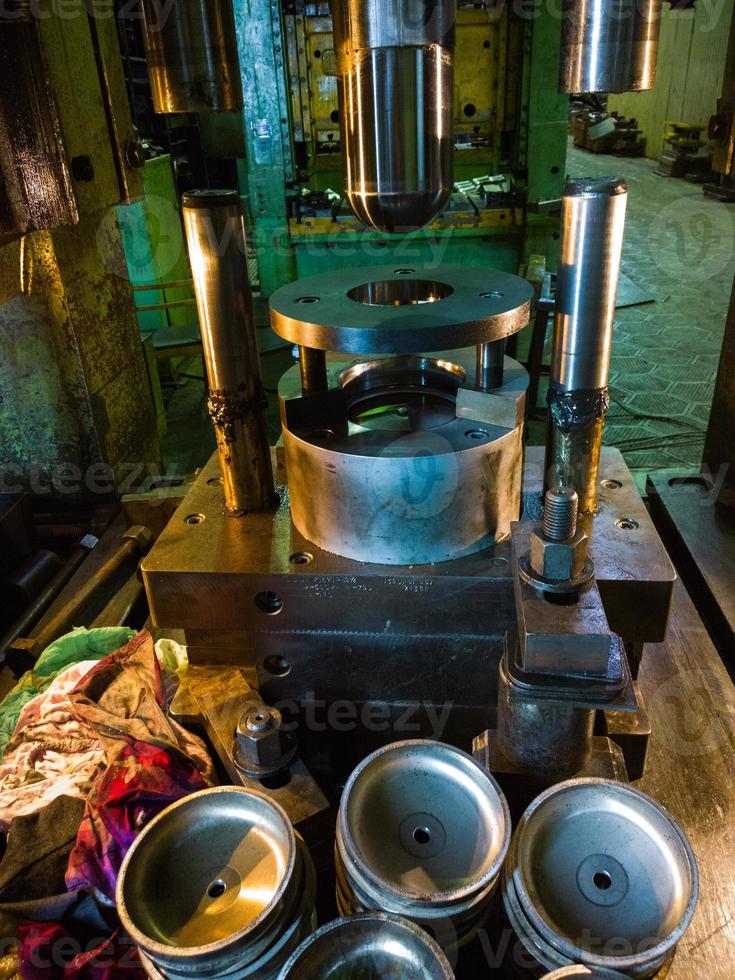 low tech stamping press producing round aliminium parts in dark environment photo