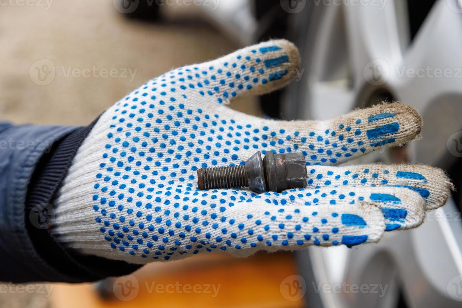mechanic hand in fabric glove holding car wheel bolt photo