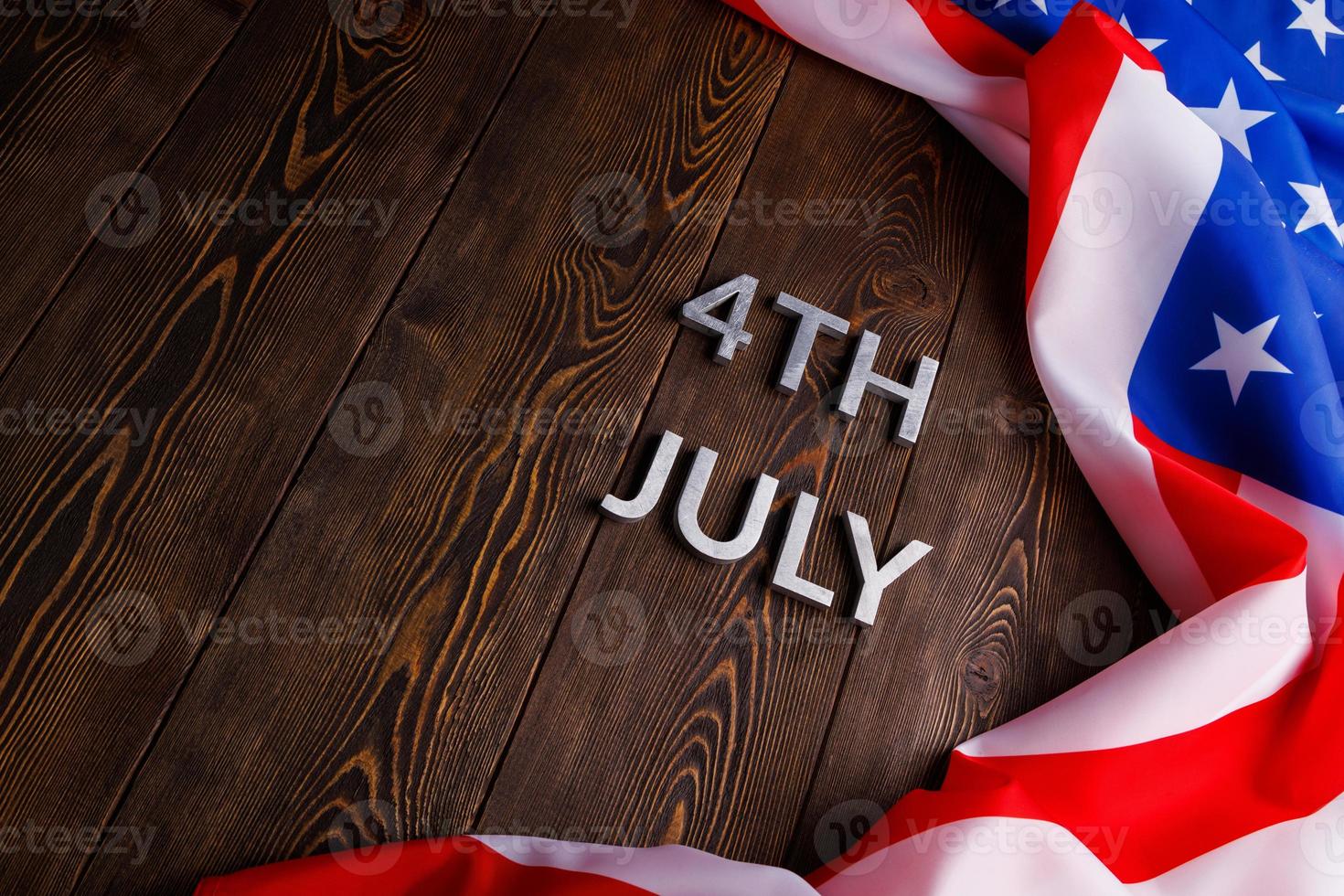 the words 4th july and crumpled usa flag on flat textured wooden surface background photo