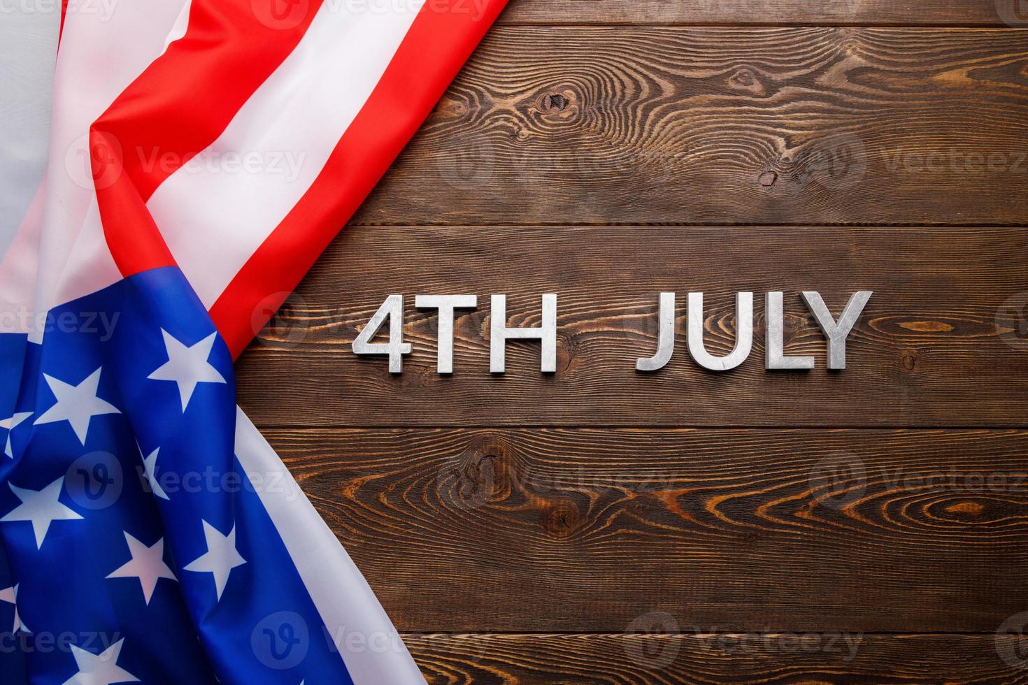 the words 4th july and crumpled usa flag on flat textured wooden surface background photo