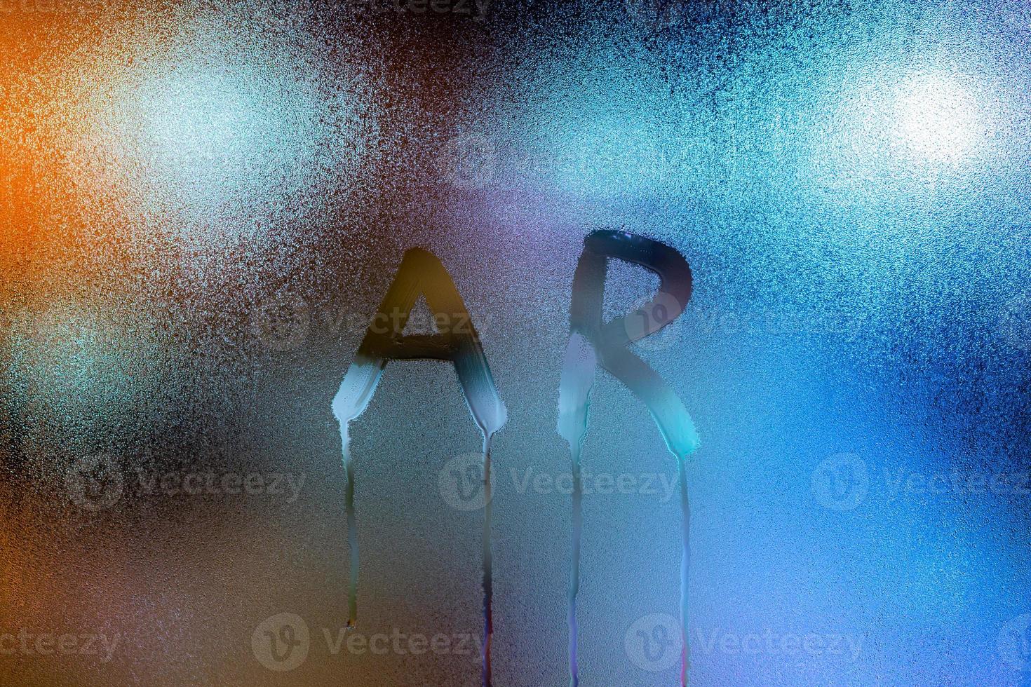 word AR - augmented reality - written by finger on wet glass with blurred lights photo
