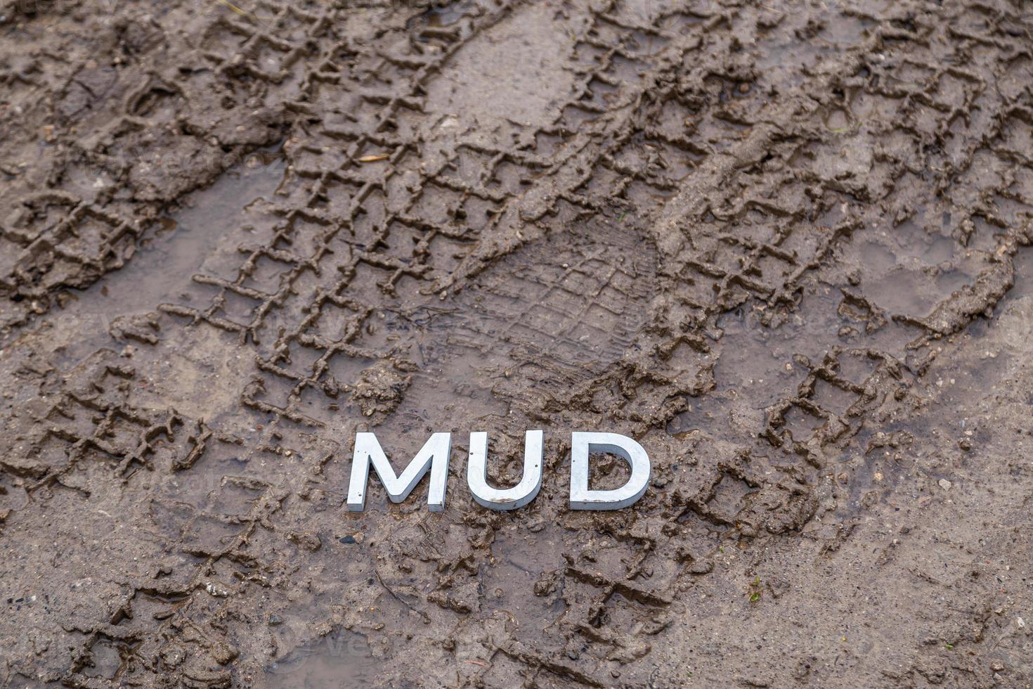 the word mud laid with silver metal letters on wet dirt surface photo