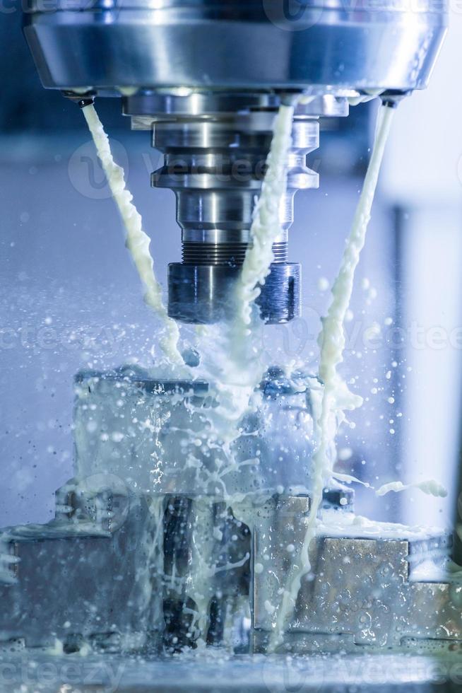 Vertical photo of industrial wet milling process in 5-axis cnc machine with coolant flow under pressure and freezed splashes