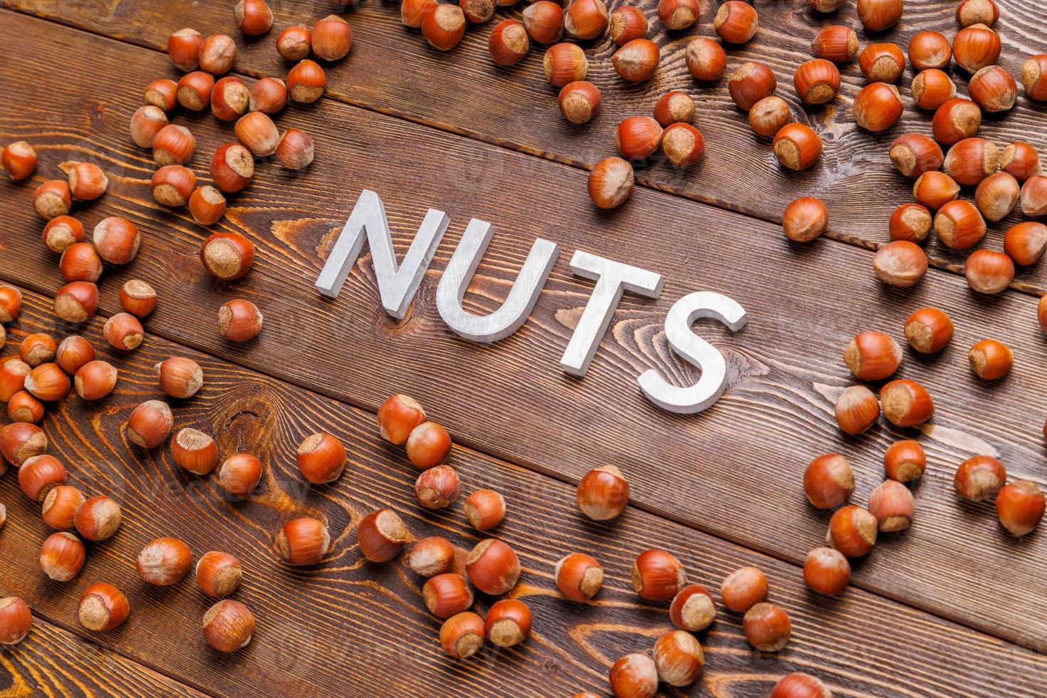 la palabra nueces colocada con letras plateadas sobre fondo de tablero de madera rodeada de avellanas dispersas foto