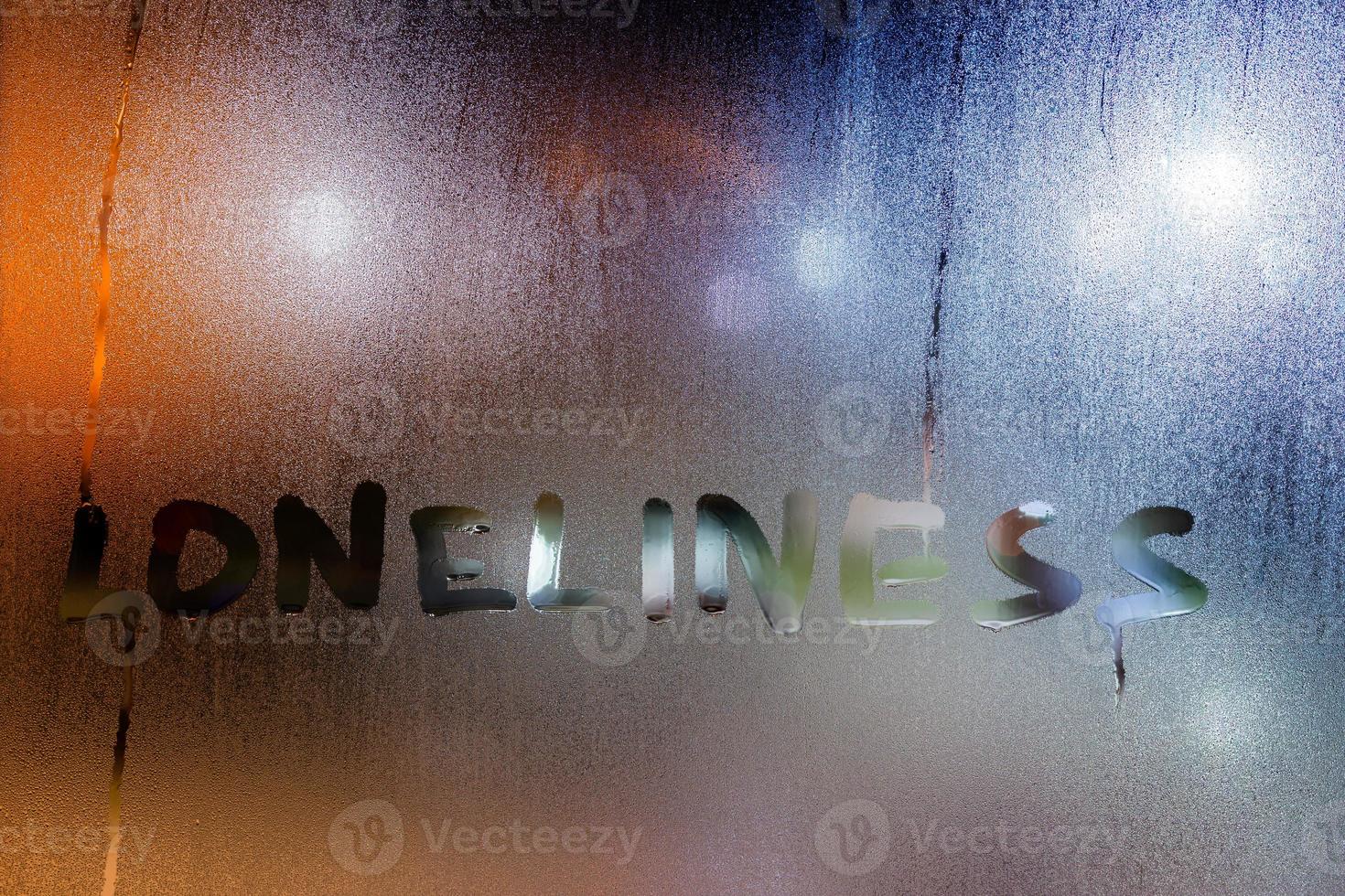 the word loneliness written by finger on night wet glass with blurred lights in background photo