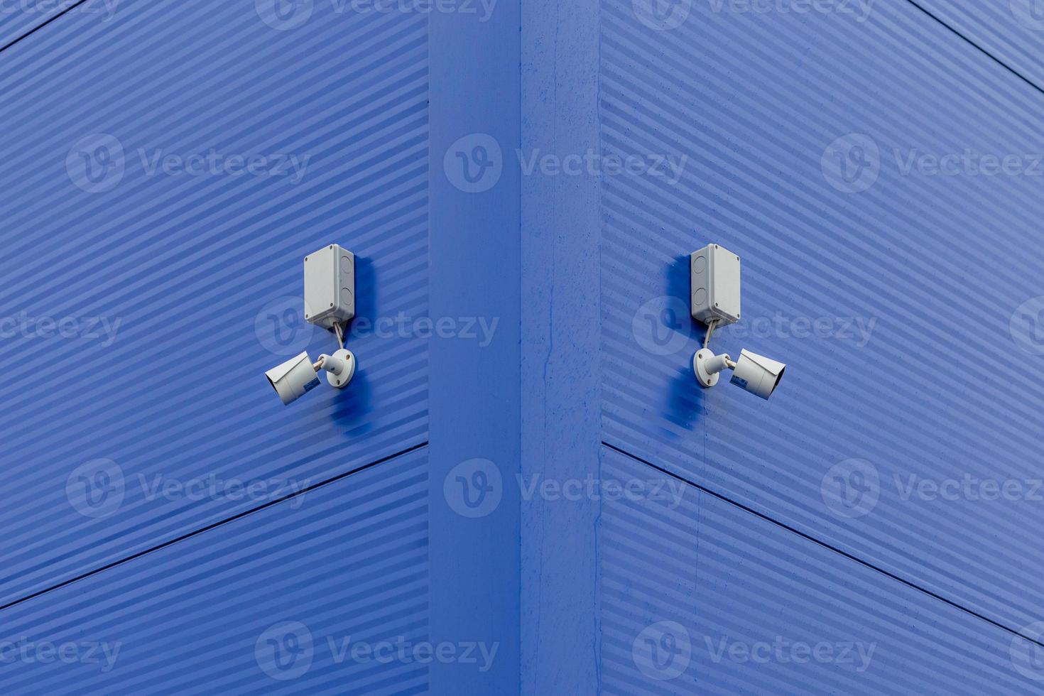 two small white security cameras on blue steel building corner photo