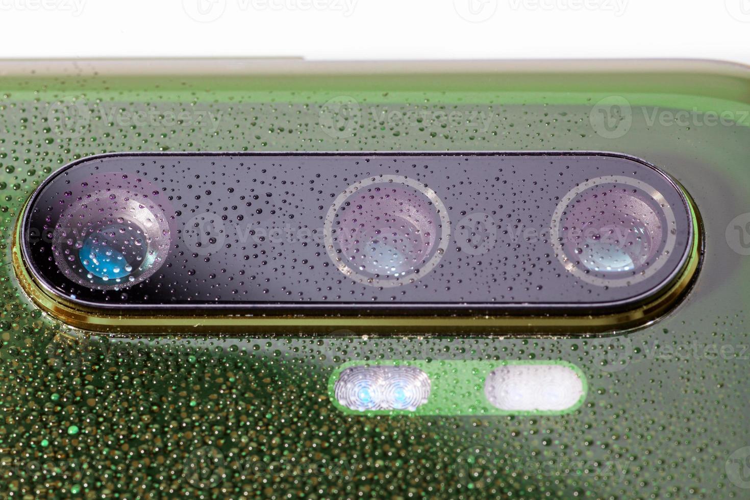 green phone camera lens covered with small water drops - close-up with selective focus and blur photo