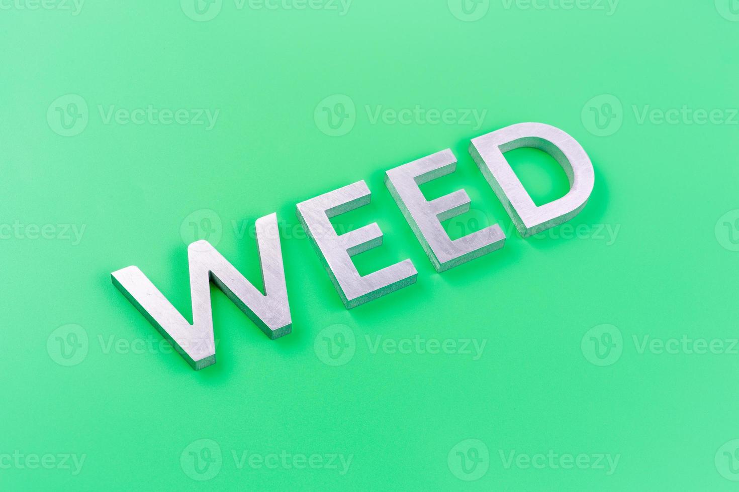 the word weed laid with silver metal letters on pastel green background with diagonal perspective photo