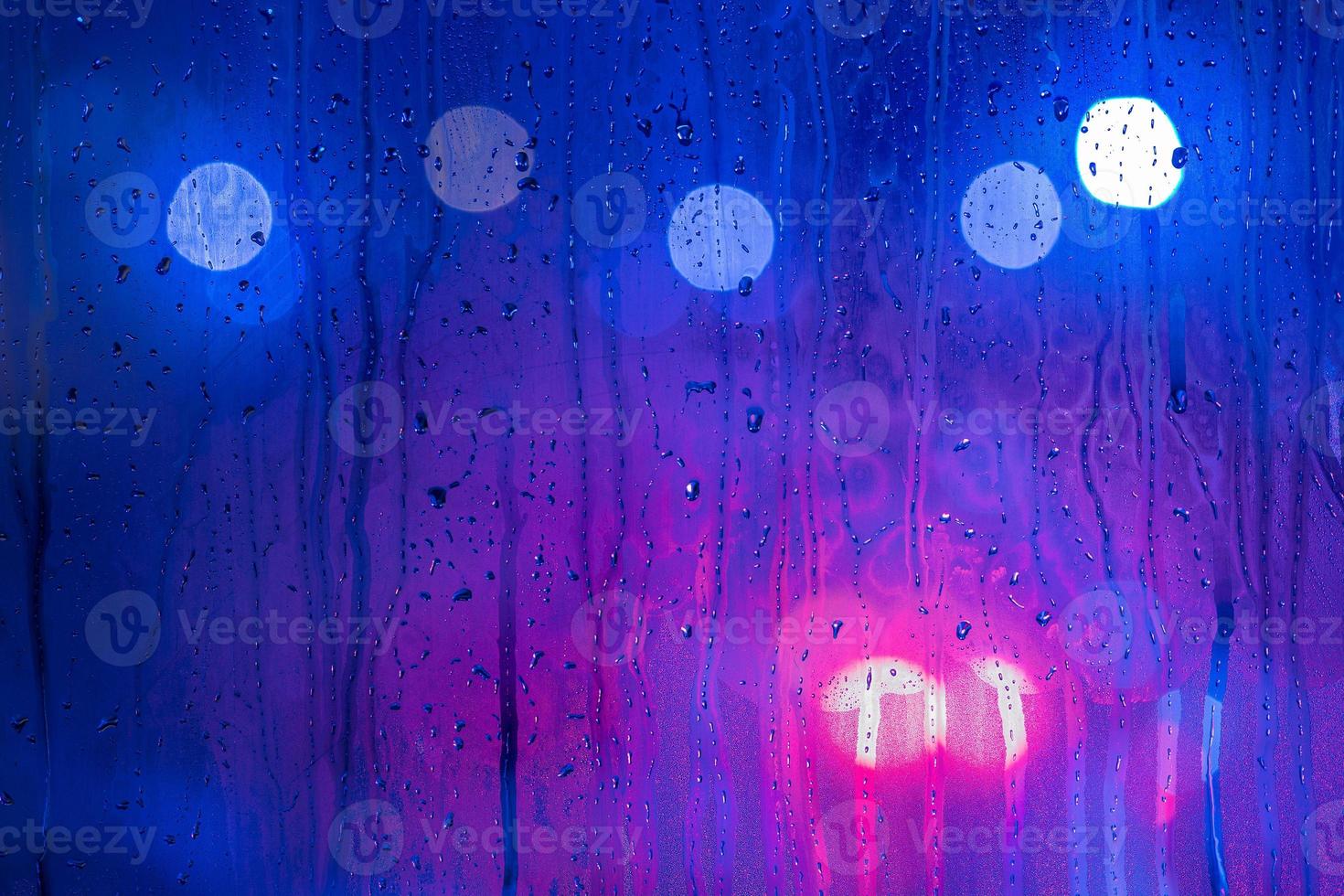 an abstract background of red, purple and blue night street lights bokeh trough wet glass with selective focus photo