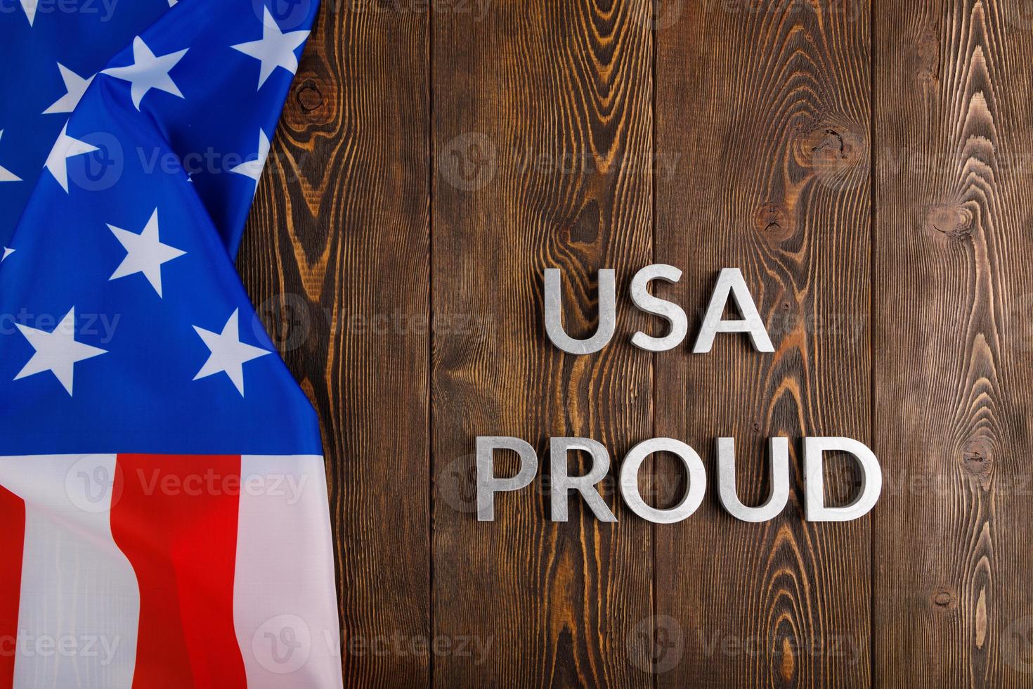 words USA proud laid with silver metal letters on brown wooden surface with flag of United States of America photo