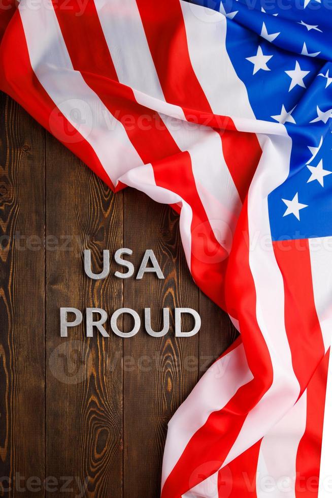 words USA proud laid with silver metal letters on brown wooden surface with flag of United States of America photo