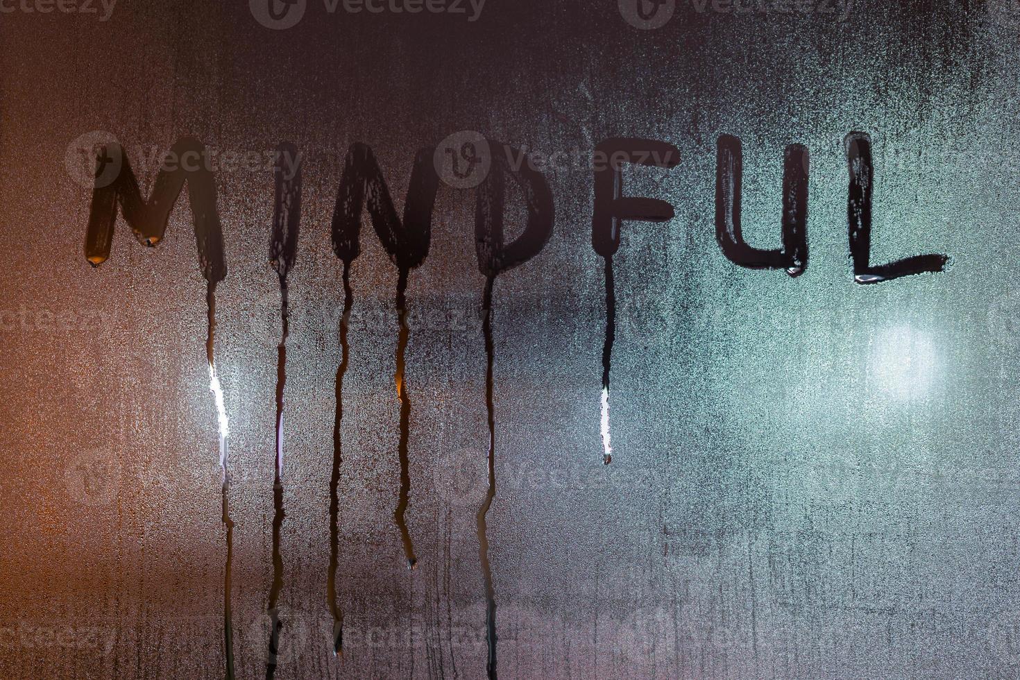 the word mindful written on night wet window glass close-up with blurred background photo