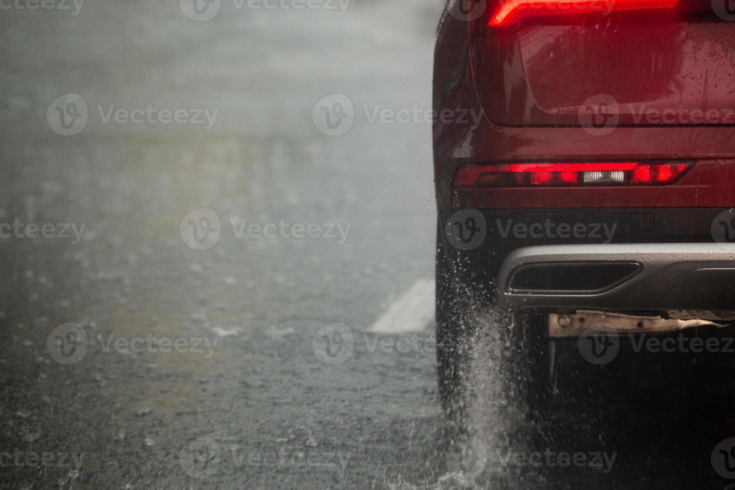 Rain water splash flow from wheels of red car moving fast in daylight city with selective focus. photo