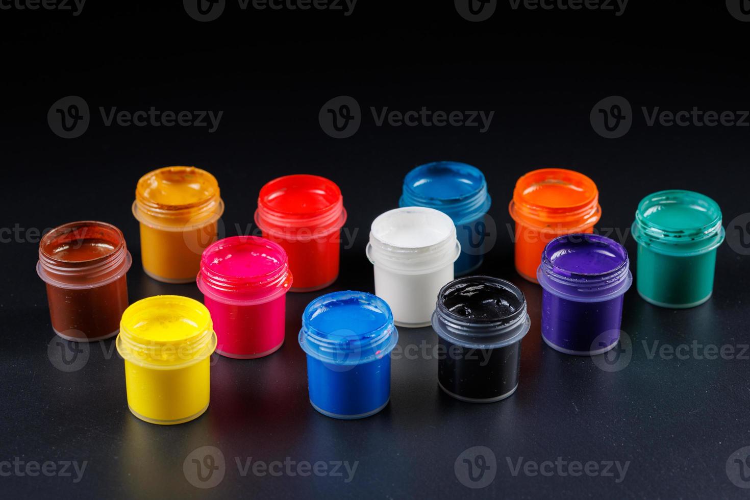 close-up background of opened small gouache paint jars on black surface photo