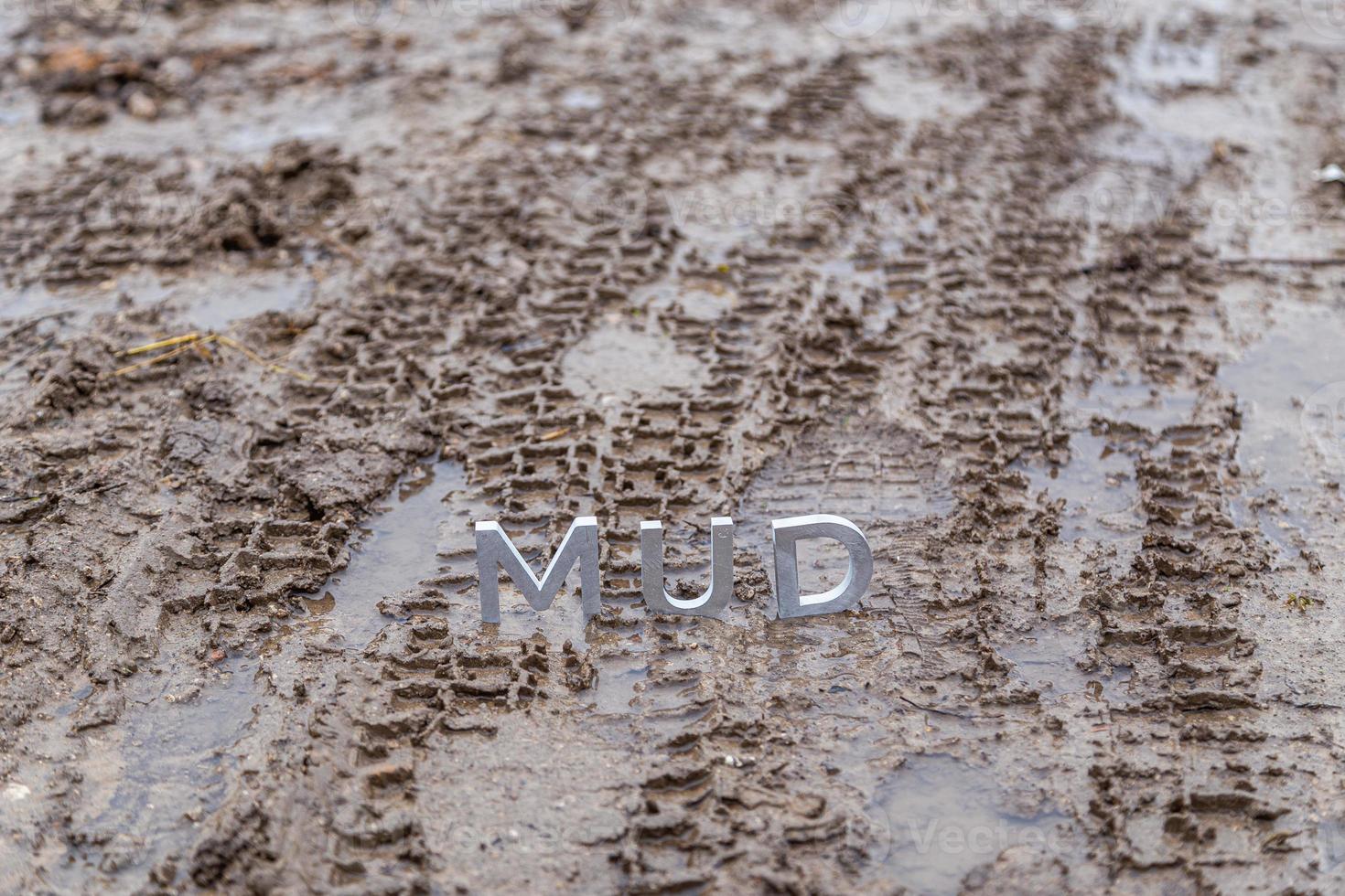 la palabra barro compuesta de letras de metal plateado en la superficie de tierra mojada foto