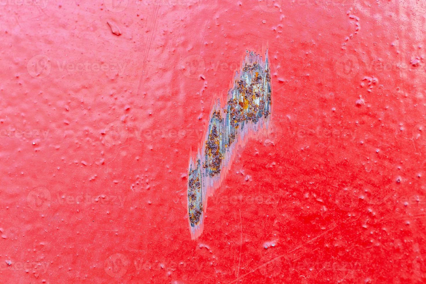 red painted metal surface with local rusted scratch - close-up with selective focus photo