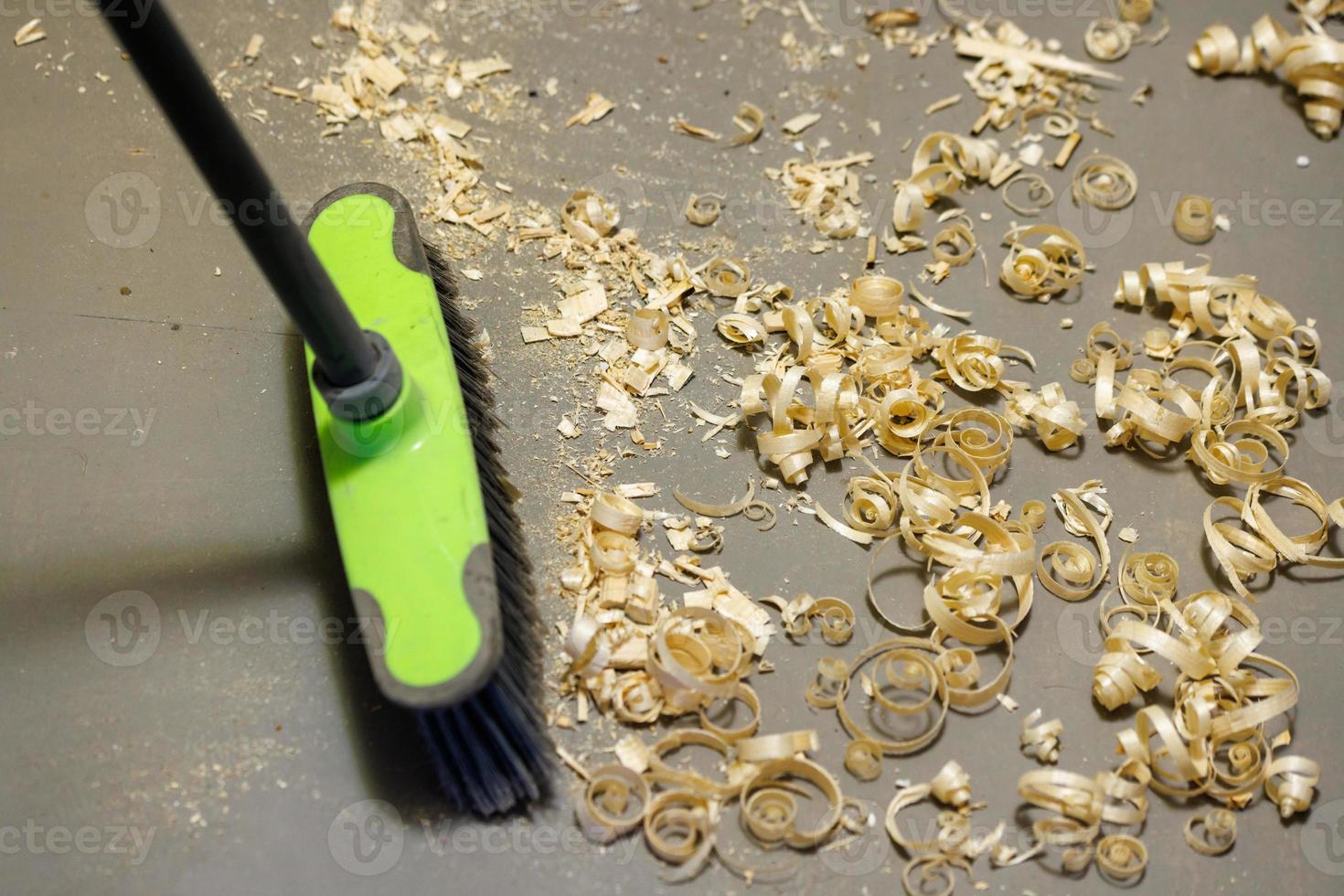 a small pile of wood shavings on a gray linoleum floor with a broom brush photo