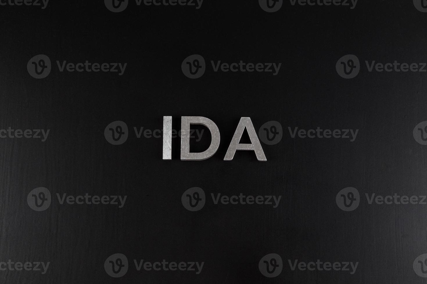 the word ida laid with silver metal letters over dry black matte surface photo