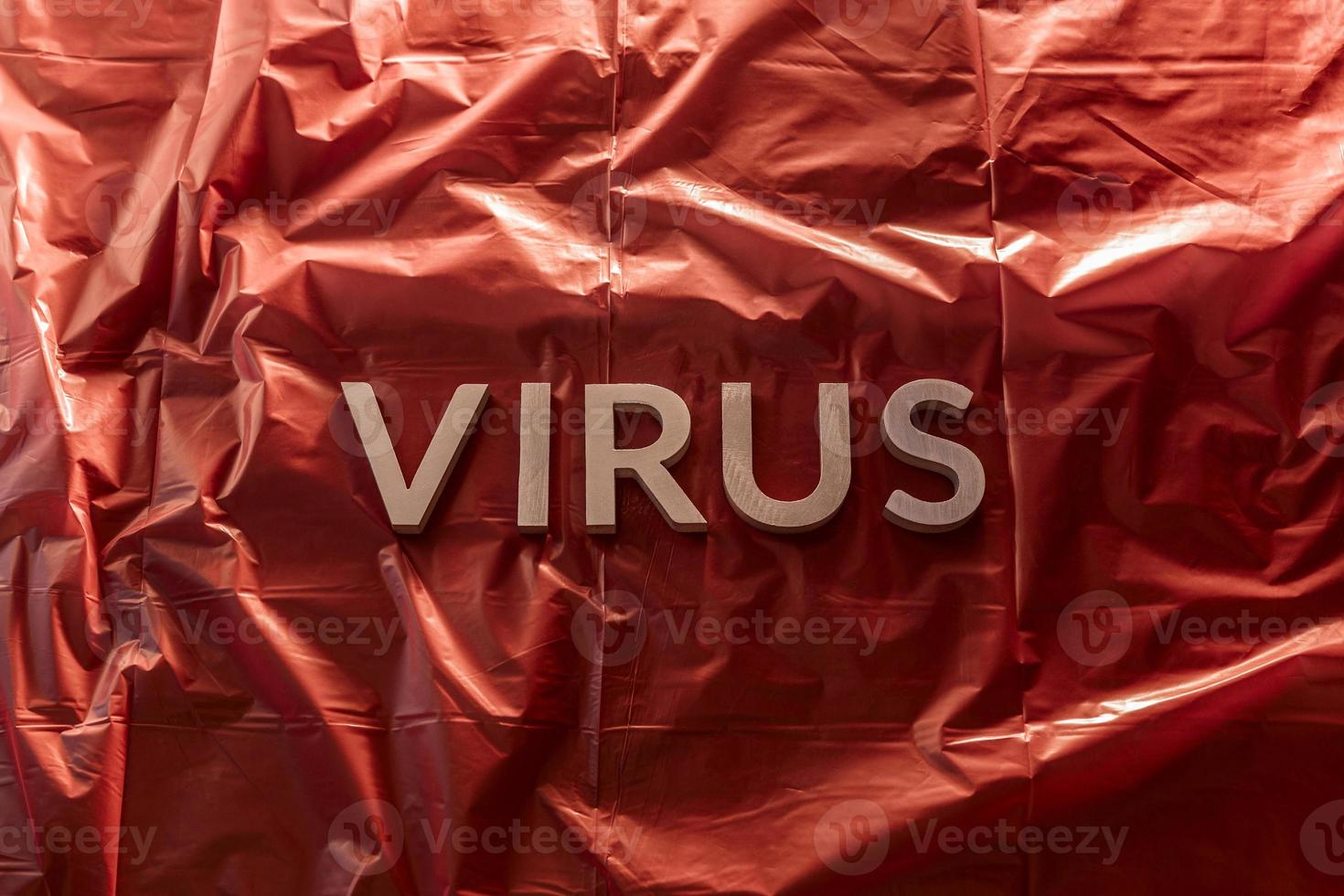 the word virus laid with silver metal letters on red background of crumpled plastic film with dramatic light photo