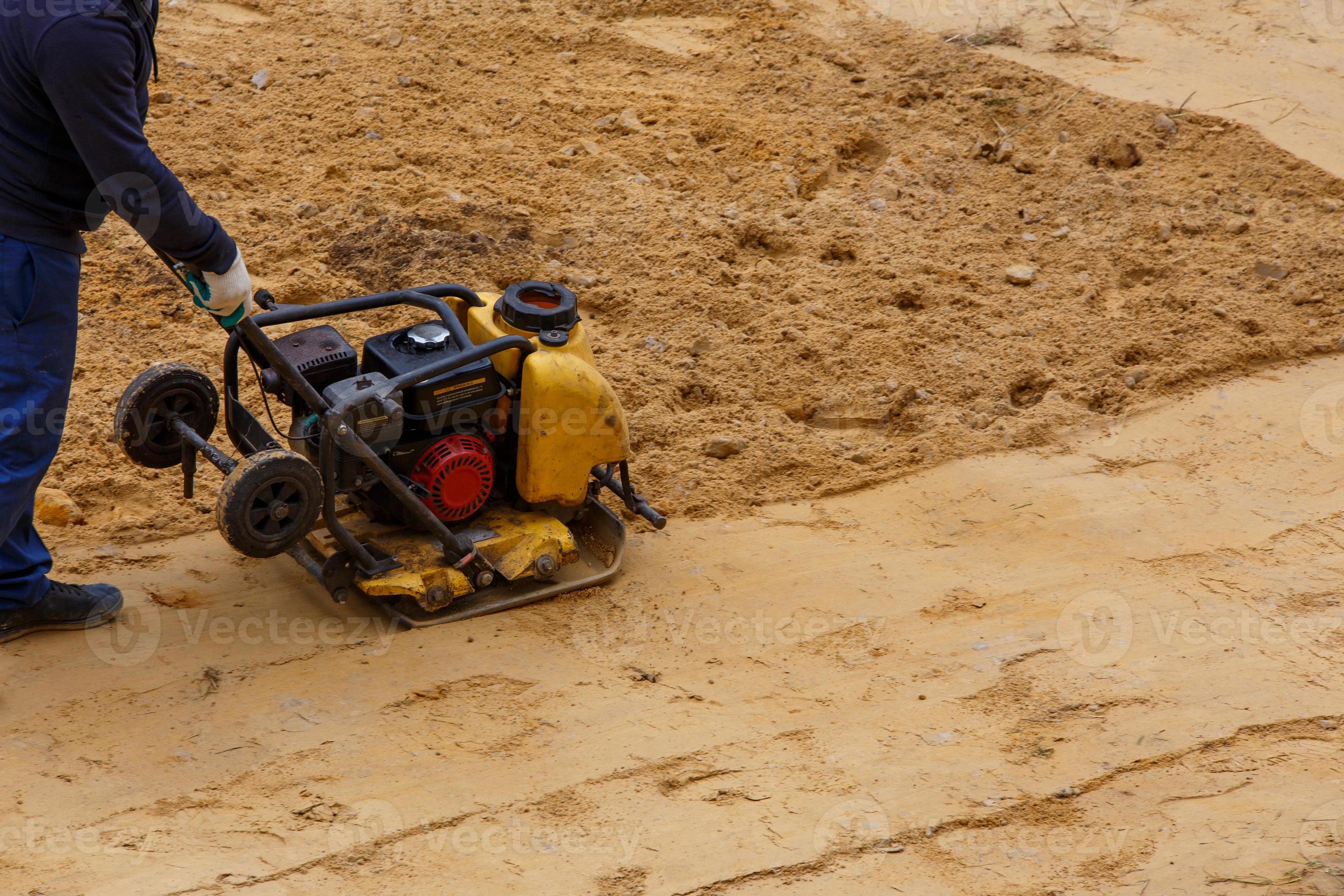 Worker in use vibratory plate compactor for compaction sand during path