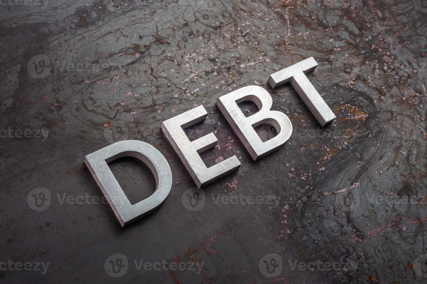 the word debt laid with silver letters on raw rusted steel sheet surface in slanted diagonal perspective photo