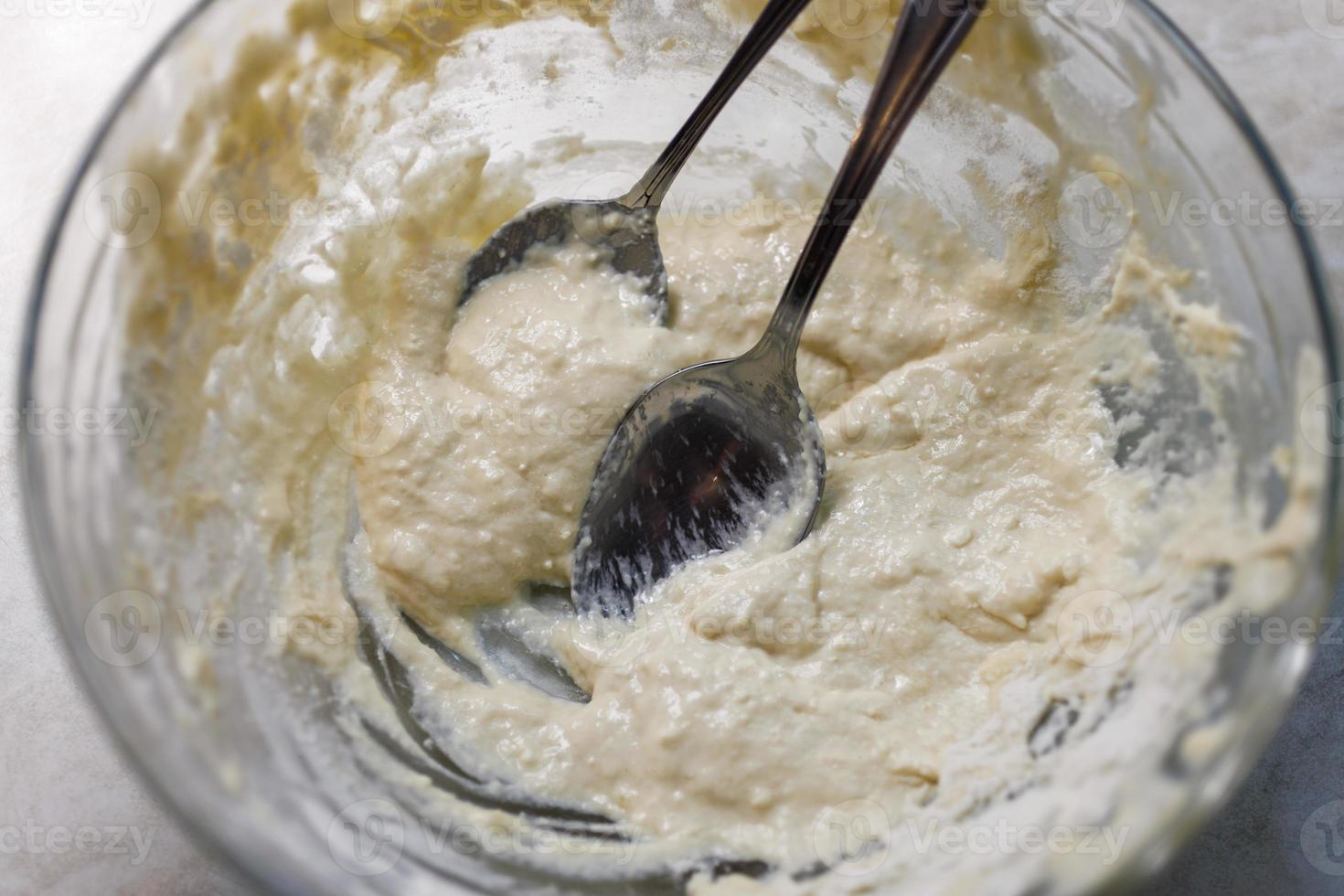 Large glass bowl with leftovers of batter and two tablespoons photo