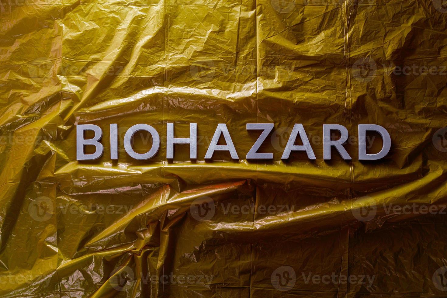 the word biohazard laid with silver letters on yellow crumpled plastic film background in flat lay composition at center photo