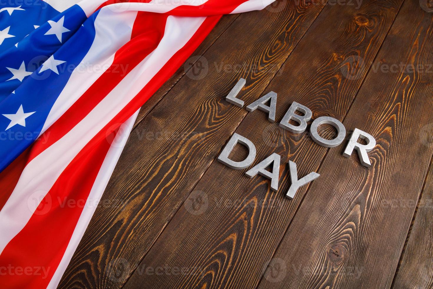 words labor day laid with silver metal letters on wooden surface with crumpled USA flag on left side photo