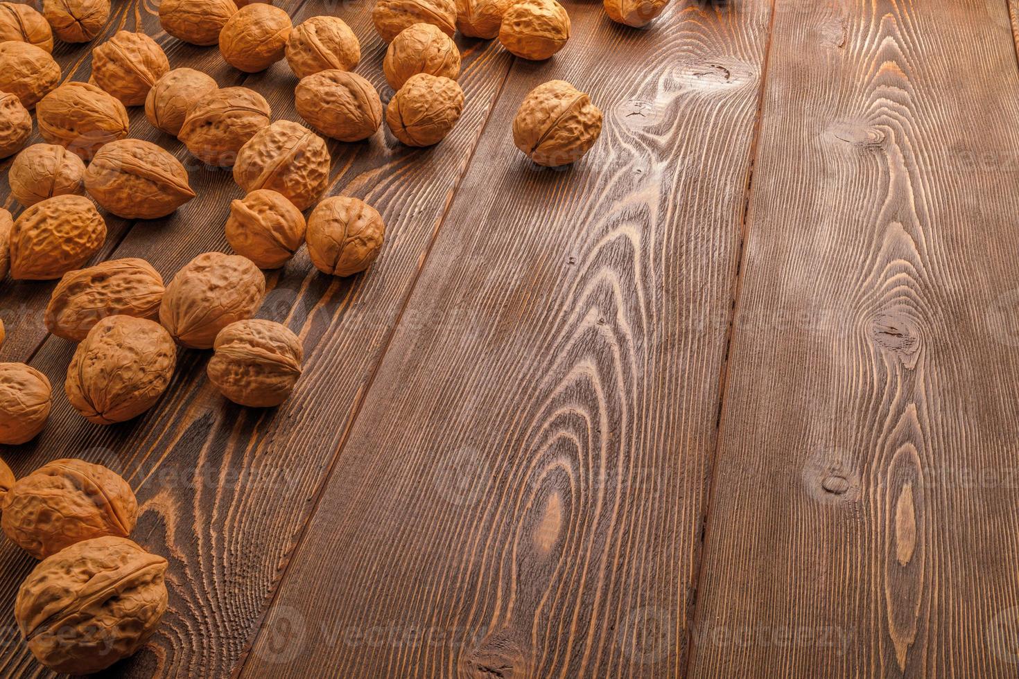 many walnuts with shells randomly scattered on brown wooden surface with copy space at right side of picture photo