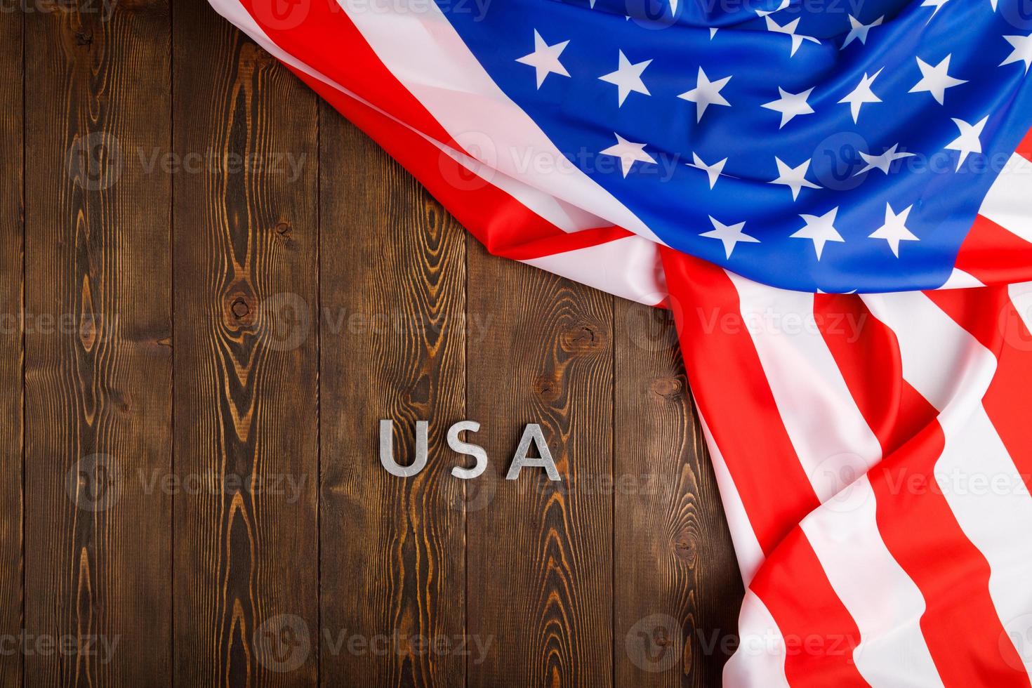 the word USA laid with silver metal letters on wooden board surface under crumpled flag of United States of America photo