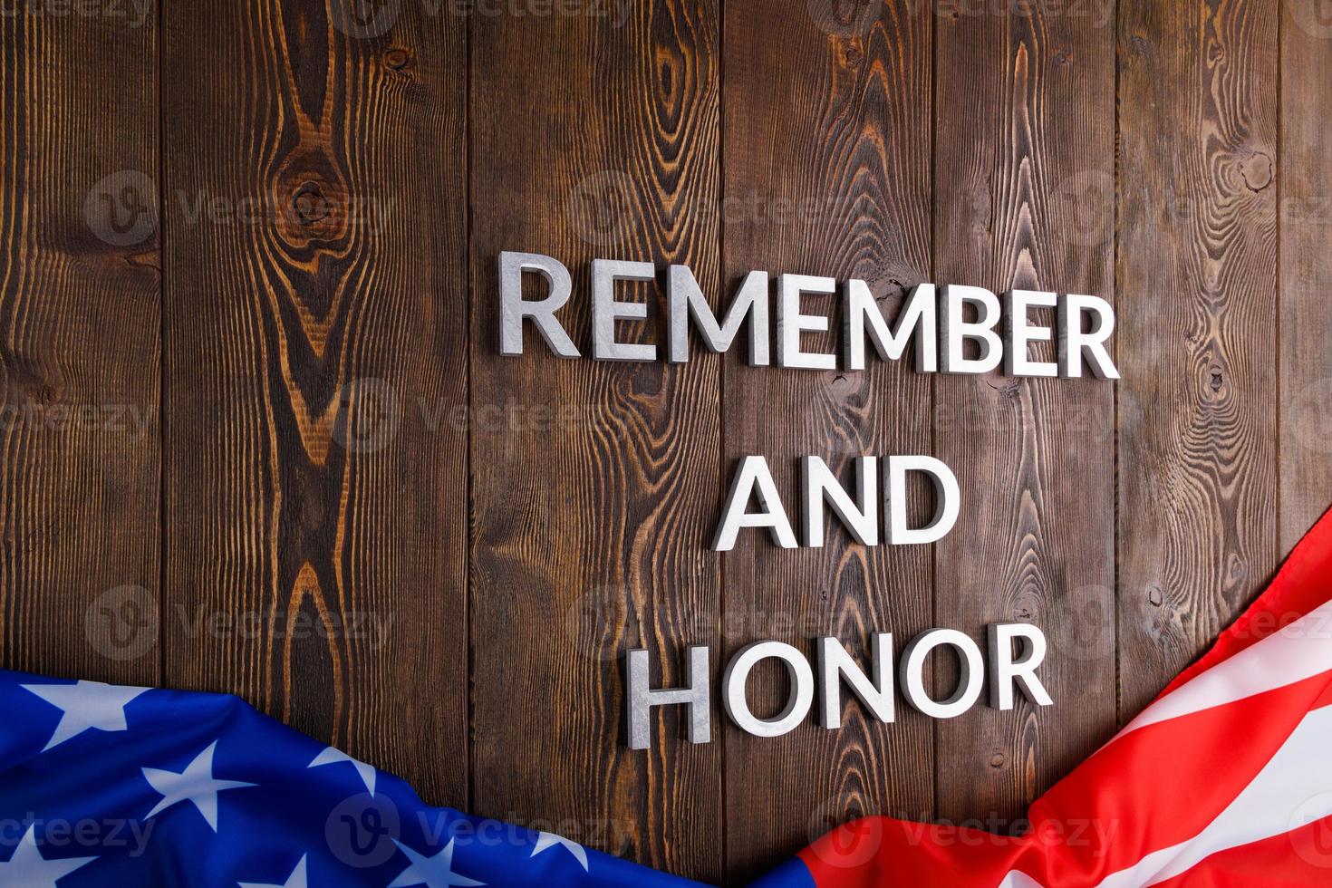 las palabras recuerdan y honran colocadas con letras de metal plateado sobre fondo de madera con la bandera de EE.UU. debajo foto