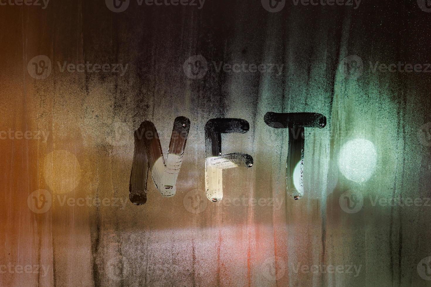 the word NFT - non-fungible token handwritten on foggy window glass at night photo