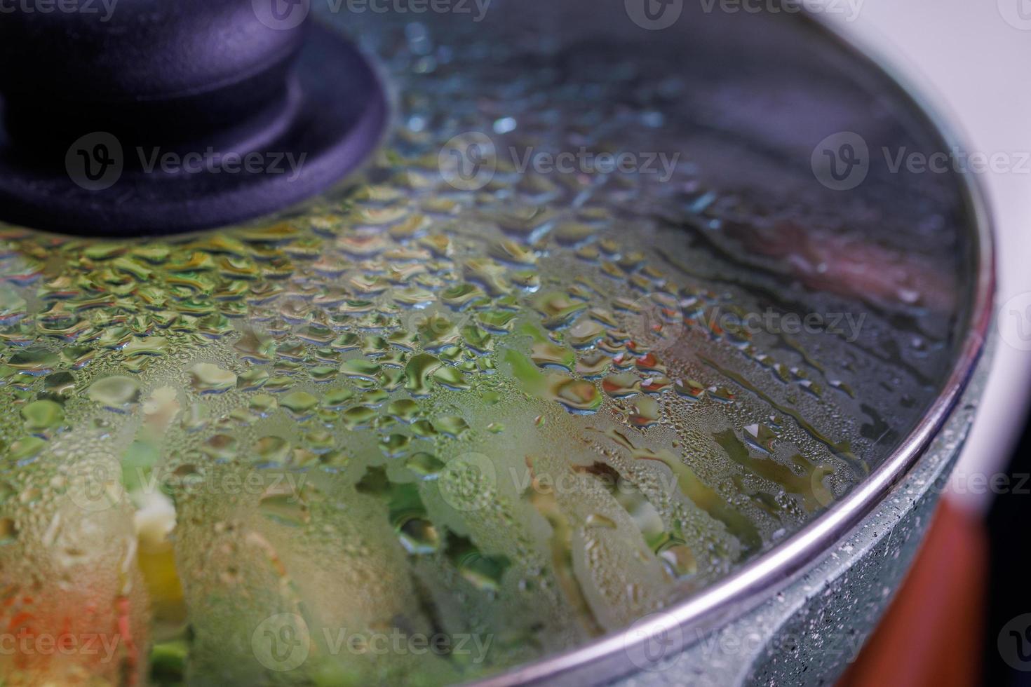 vegetables in frying pan covered with glass lid with water condensation drops on inner surface photo