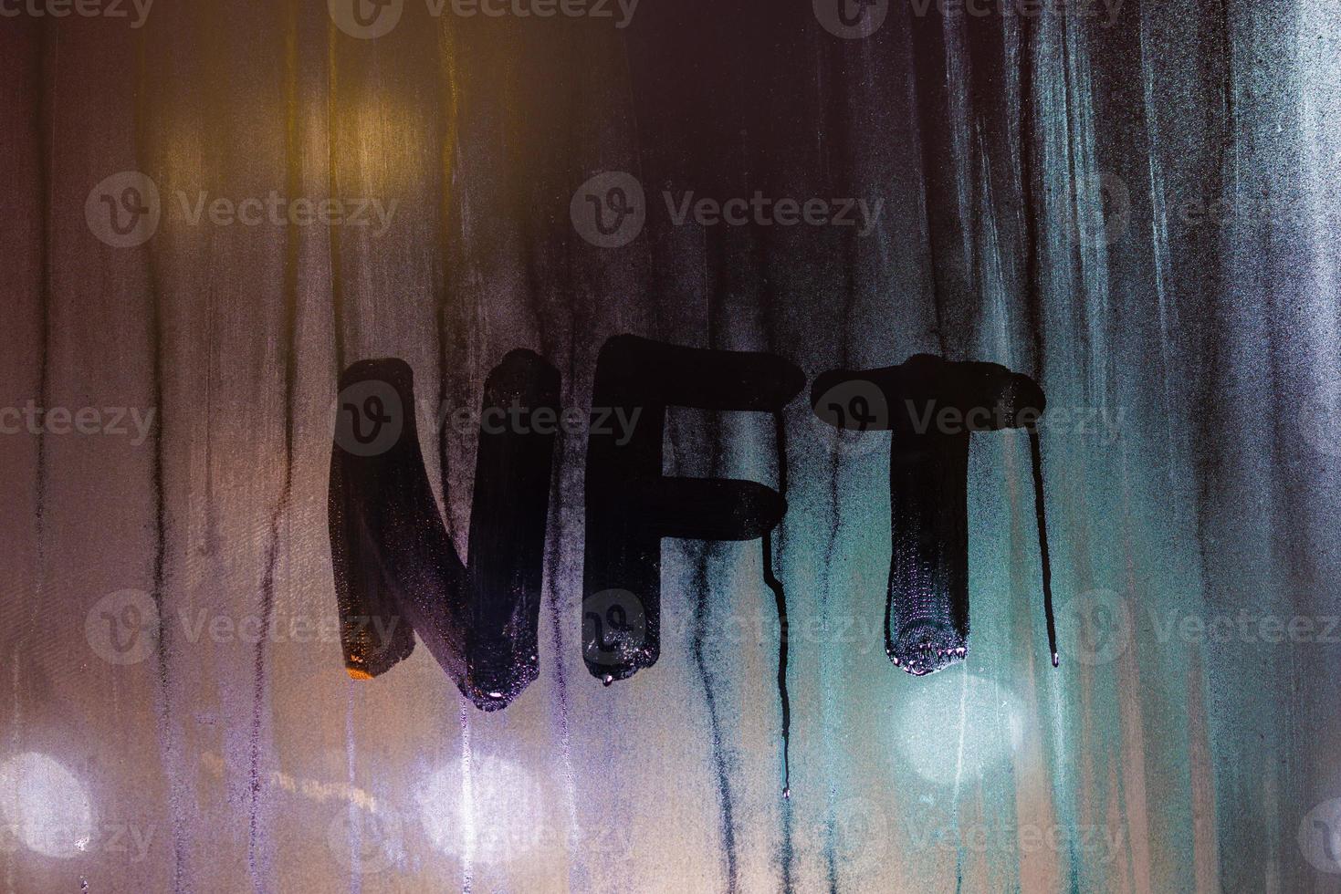 the word NFT - non-fungible token handwritten on foggy window glass at night photo