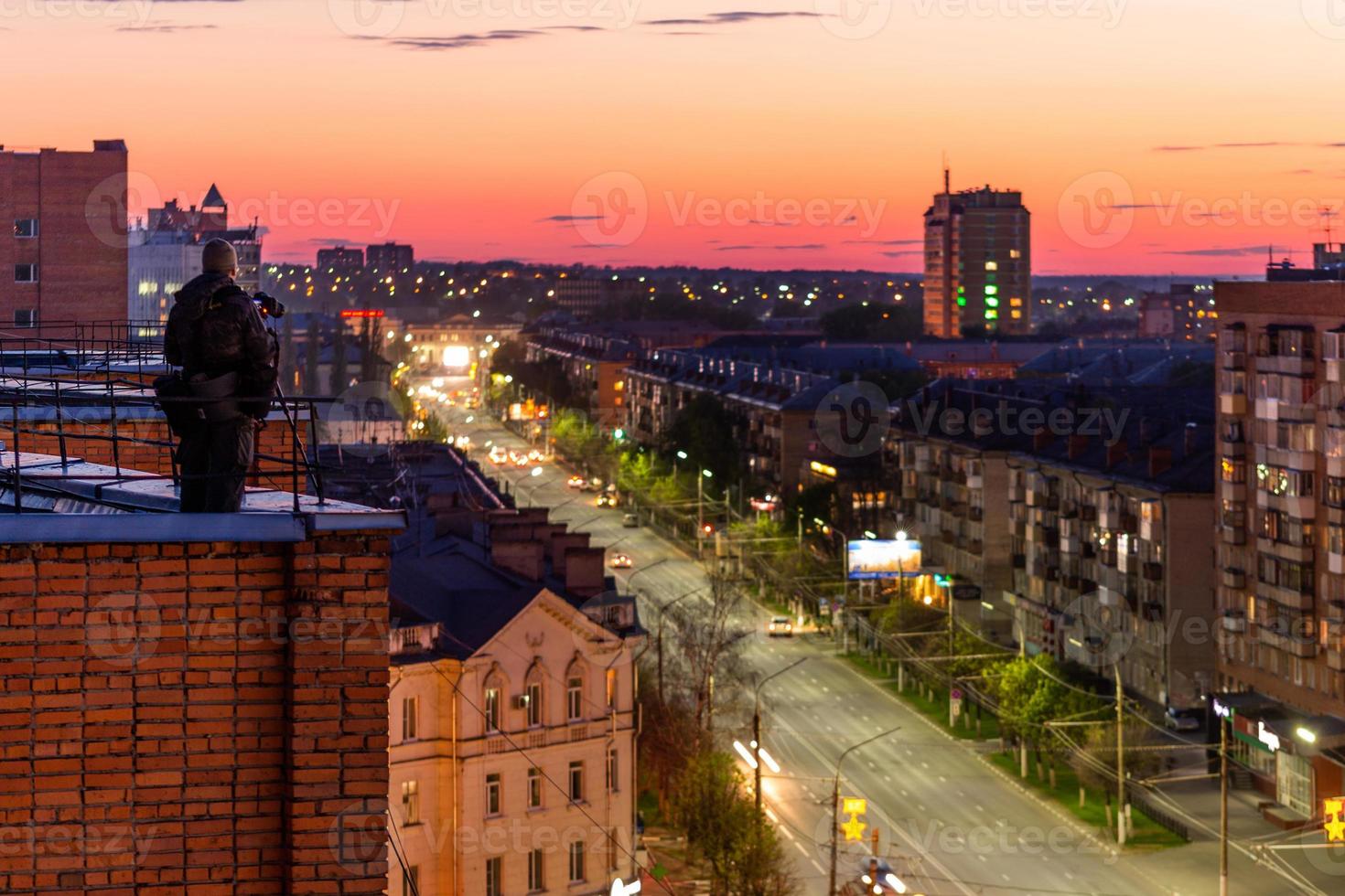 photographer shooting night sity from edge of red brick condominium roof photo