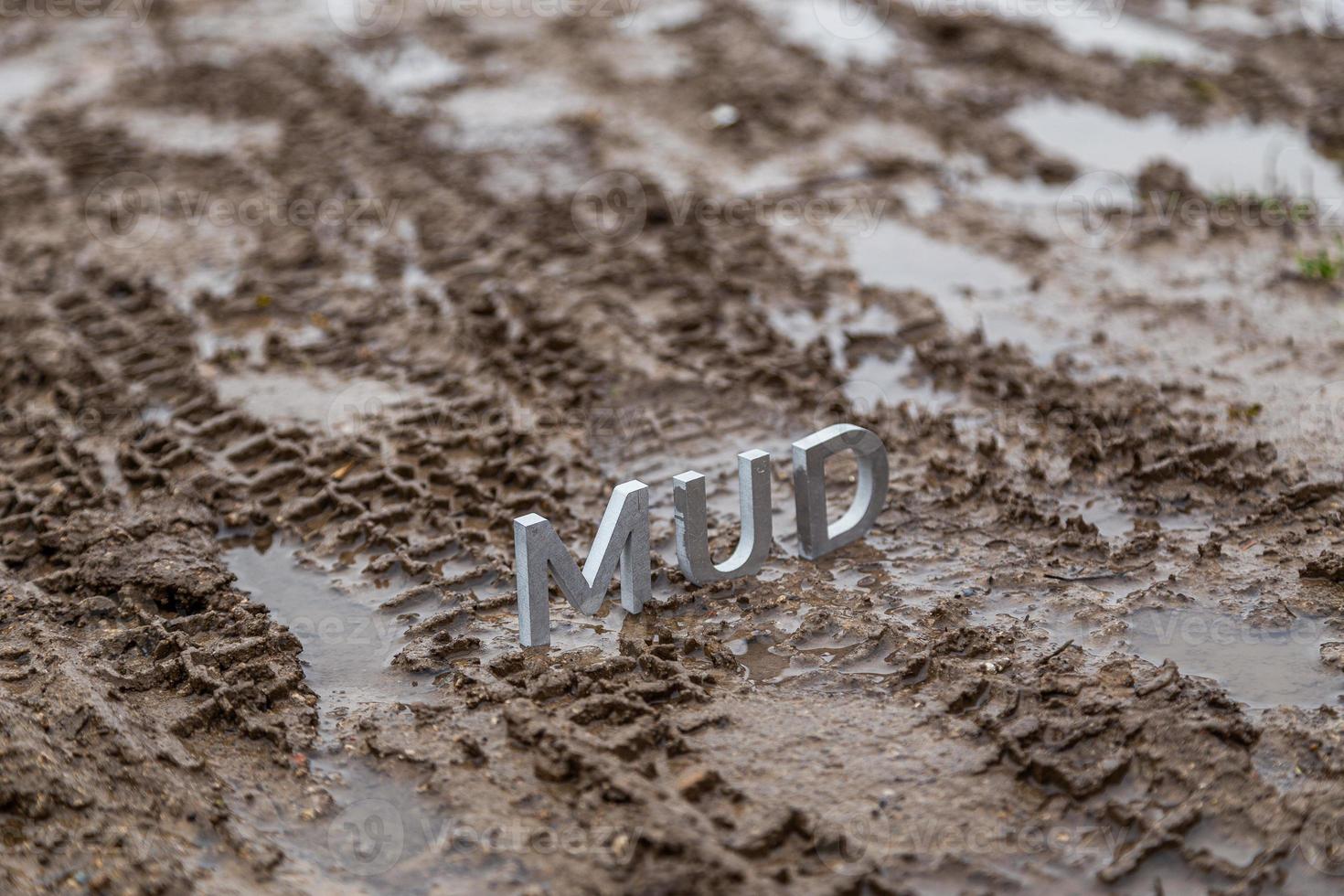 the word mud composed of silver metal letters on wet dirt surface photo