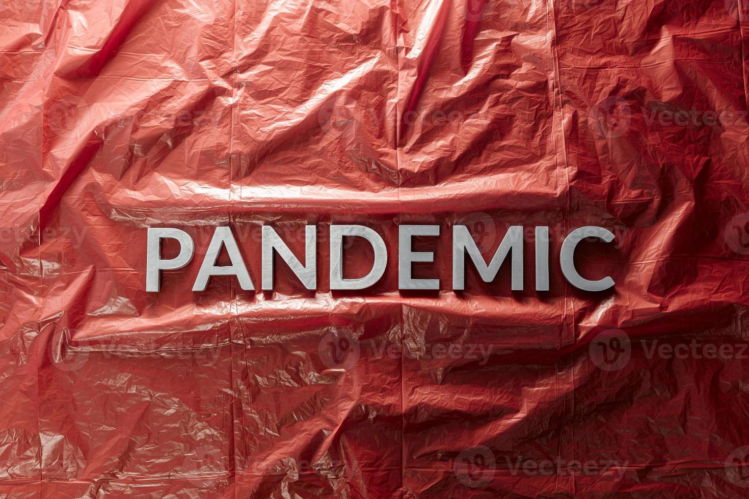 the word pandemic laid with silver letters on red crumpled plastic film background in flat lay composition at center photo