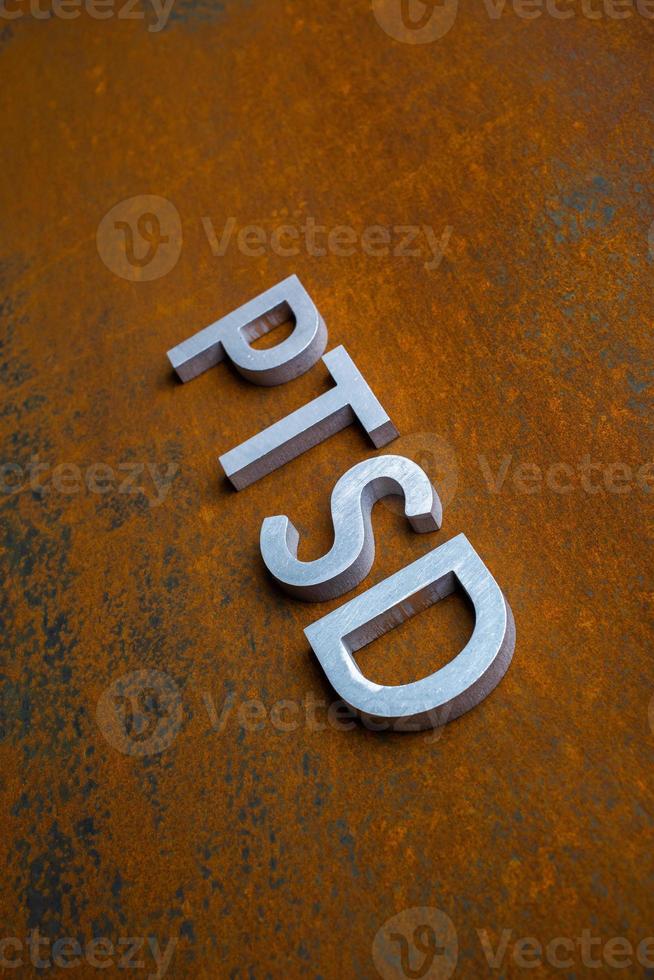 la palabra ptsd colocada con letras de metal plateado sobre fondo plano de chapa de acero oxidado en perspectiva diagonal inclinada foto