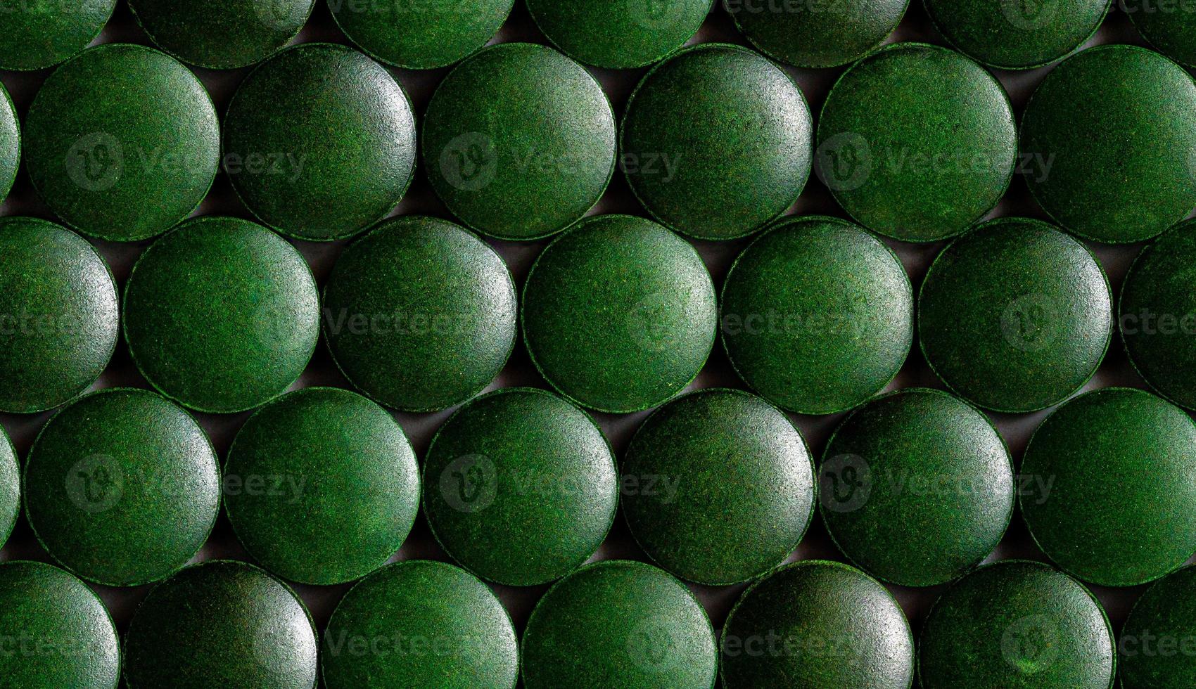 un patrón hexagonal sin costuras de muchas tabletas de espirulina orgánica verde colocadas apretadas en una capa sobre una superficie plana foto