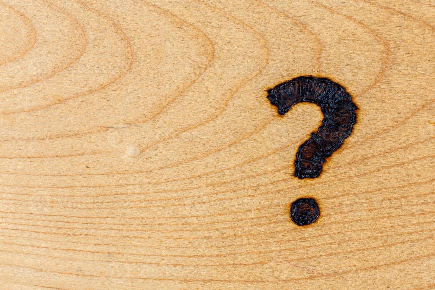 question mark drawn with handheld woodburner on bright flat wooden surface photo