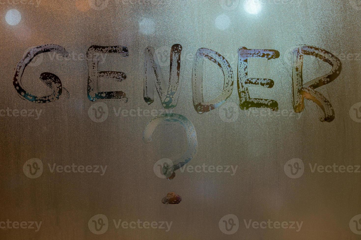 the question gender written by finger on night wet glass with blurred lights in background photo