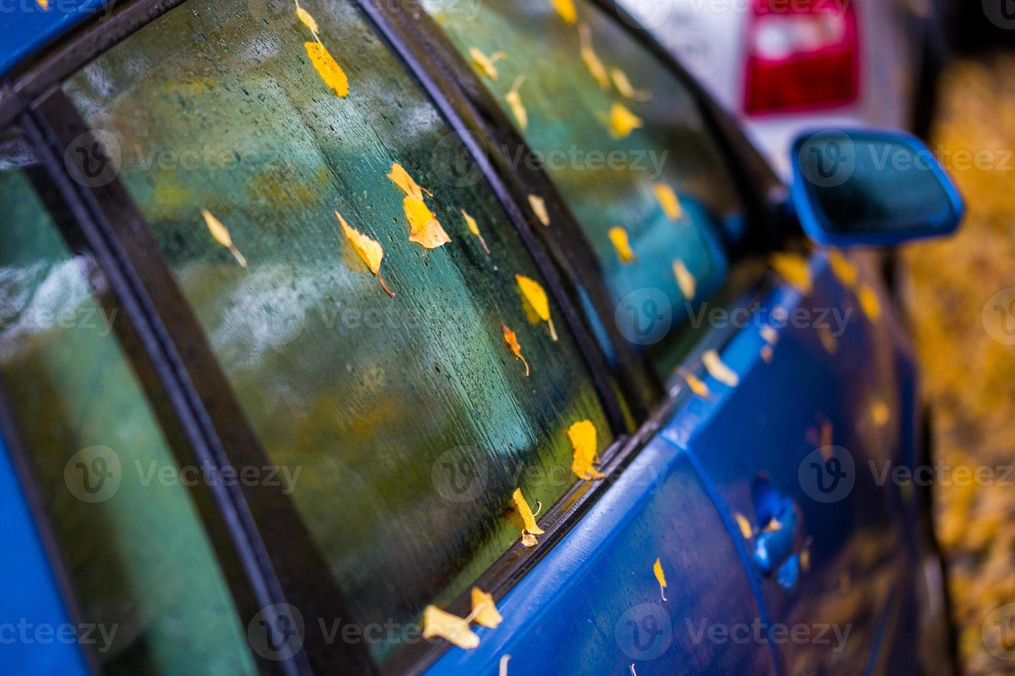 lado húmedo del coche azul ultramar con hojas de otoño y enfoque selectivo foto